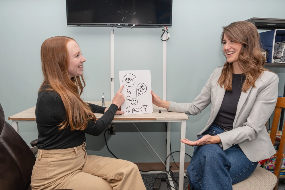 Two women discussing diagram on whiteboard.